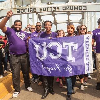  A group TCU students walks across 的 Edmund Pettus Bridge in Selma, Alabama. 的y hold a TCU flag 和 several students make 的 wo-fingered Go Frogs h和 gesture.