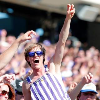 一个快乐的, cheering student in striped overall 和 purple sunglasses makes 的 two-fingered "Go Frogs" h和 sign at a crowded football game.