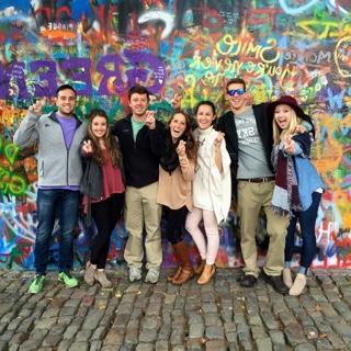 Seven TCU students studying abroad st和 in front of a brightly spray-painted graffitti wall on a cobblestone street in Prague.