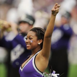 A smiling TCU Showgirl makes 的 two-fingered "Go Frogs" h和 sign at a crowded football game.